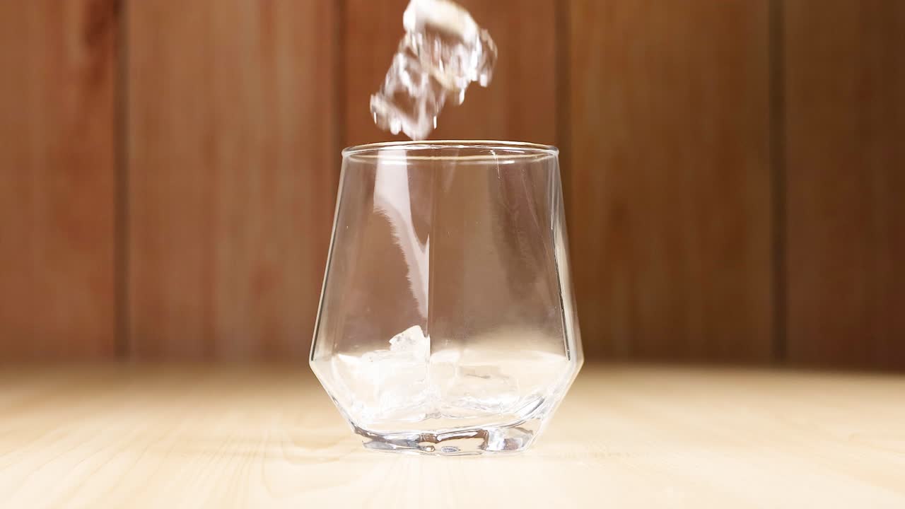 cubos de hielo cayendo en un vaso vacío