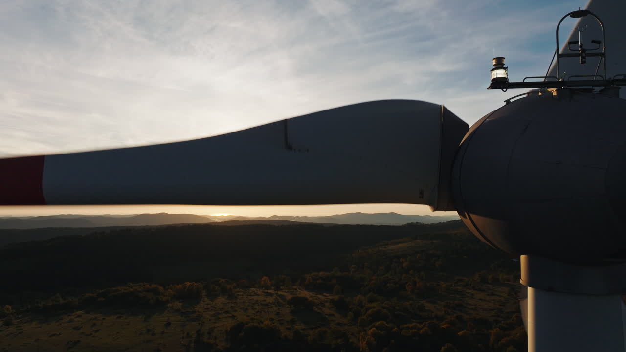 Luftfoto viser en moderne vindturbin ved solnedgang med gyllent lys og en dramatisk himmel i
