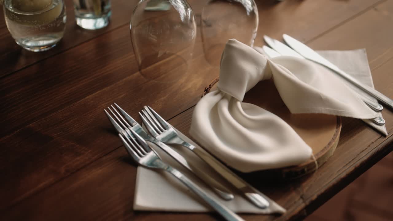 Close-up shot of neatly arranged silverware, folded napkins, and glassware on a wooden dining table, in soft natural light