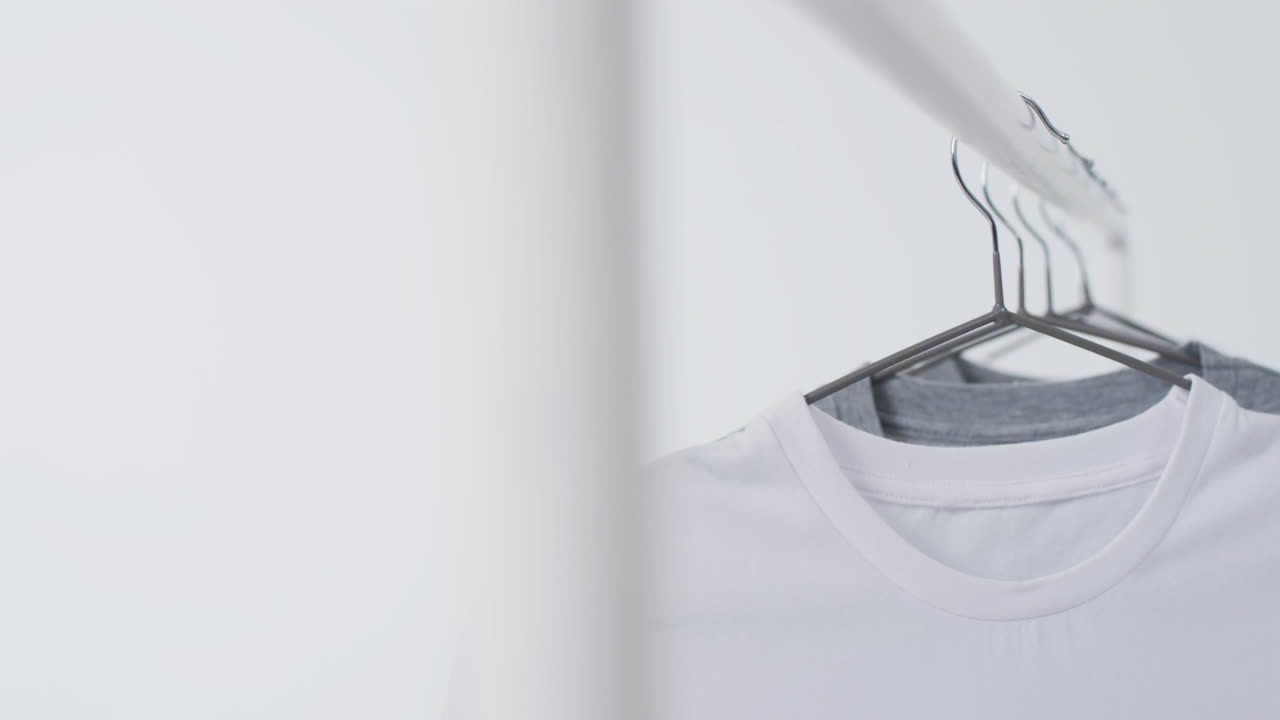 Video of white and grey t shirts on hangers and copy space on white background