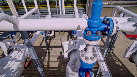 industrial pipelines with blue valves and a red-handled lever are arranged within a paved processing facility - pan right shot
