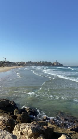 Jaffa old historic city and Tel Aviv beach in summer day outdoors. Phone UGC footage of sunny day during vacation as waves crash on shore by promenade along coast of modern and old city in Israel
