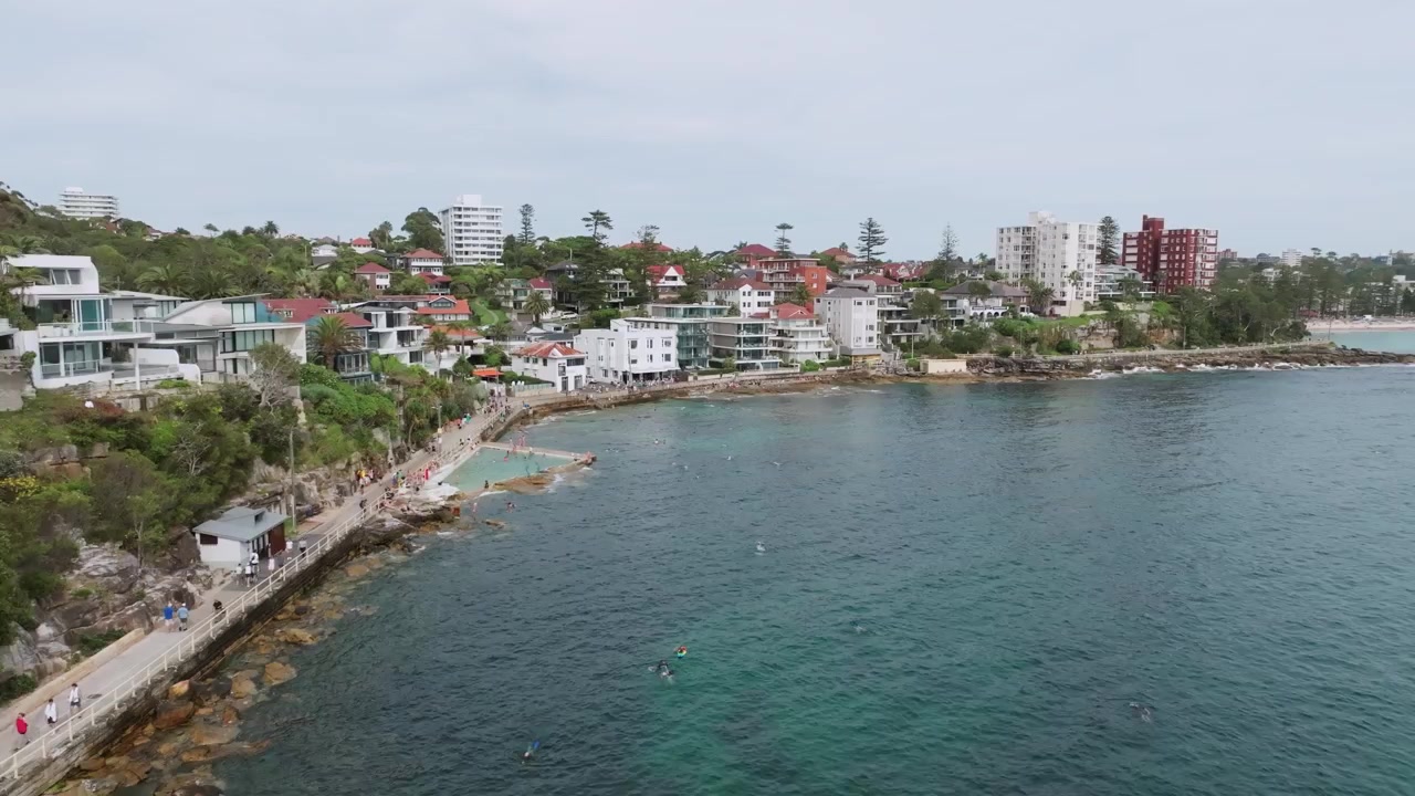 Volo cinematografico di drone lungo il lungomare di Shelly Beach che rivela l'oceano cristallino, la passeggiata costiera, le case di lusso e la costa del porto di Sydney a Manly, Australia.