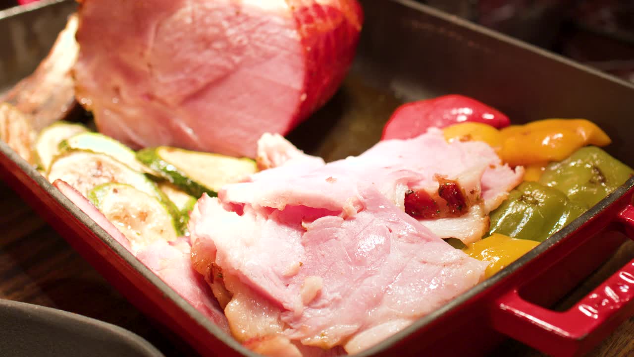 Primo piano di fette di prosciutto arrosto con zucchine e peperoni in una padella rossa