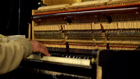 hands of old man in subway underground playing piano with opened mechanism og strings and hammers