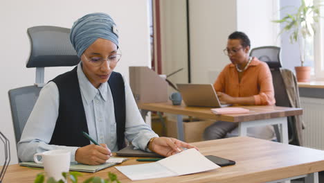 Close-Up-View-Of-Muslim-Businesswoman-Taking-Notes-And-Businesswoman-In-The-Background-1