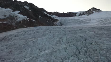 Patrones-Interesantes-Y-Hermosos,-Líneas-Y-Grietas-En-El-Hielo-Del-Glaciar-En-La-Cima-De-La-Montaña-De-Los-Alpes-Suizos-Durante-Un-Amanecer-O-Atardecer-En-El-Fondo