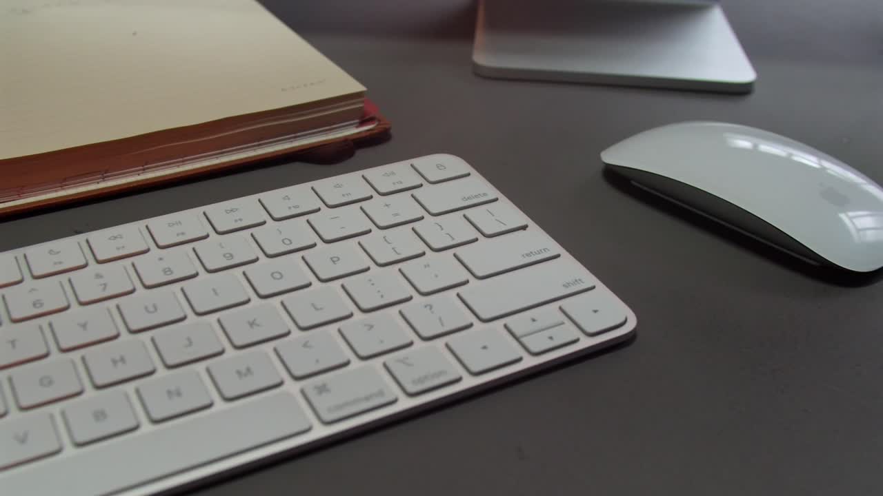 Modern Workspace With White Wireless Keyboard And Matching Mouse, With Open Planner On Desk. closeup, panning shot