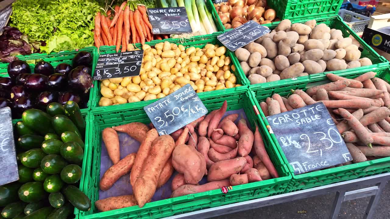 Colorful display of fresh organic vegetables at a French market stall. Crates filled with sweet potatoes, zucchini, carrots, potatoes, and eggplants with handwritten price tags