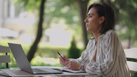 talented serious woman brunette arab hispanic ethnic group sits at a table in a summer cafe with a laptop. considers solving problems. puzzled business woman. portrait of a beautiful business woman