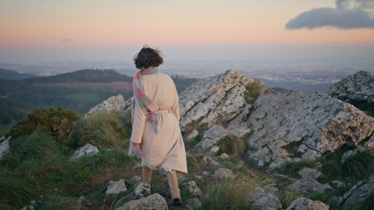 Turista che cammina su sentiero di montagna al crepuscolo indossando un cappotto. Elegante donna esploratrice