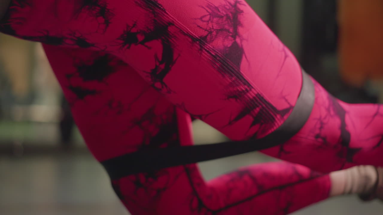 Atleta donna con leggings rosa che esegue slanci dei glutei con resistenza dell'elastico su tappetino, atmosfera di allenamento dinamica, luci da studio e attrezzatura sfocata, movimento dinamico, serie ad alta intensità per la forza.