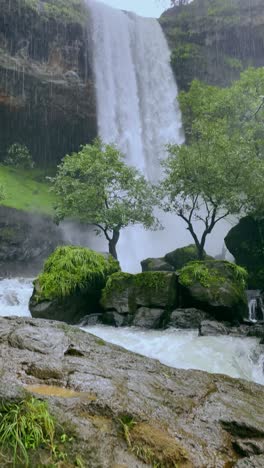 tilt-down shot of vasundhara falls in bhandardhara, maharashtra, cascading amidst lush green fields, misty mountains, and thick monsoon fog nature's raw beauty in full glory