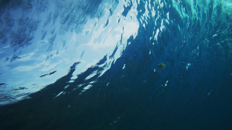 I raggi del sole penetrano la superficie dell'oceano mentre un vortice d'onda forma uno spruzzo schiumoso bianco, angolazione subacquea.