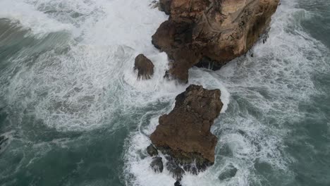 Pullback-from-Nazare-Promontory-revealing-Ocean-waves-crashing-into-Rocks,-a-Famous-Surf-spot-In-Portugal