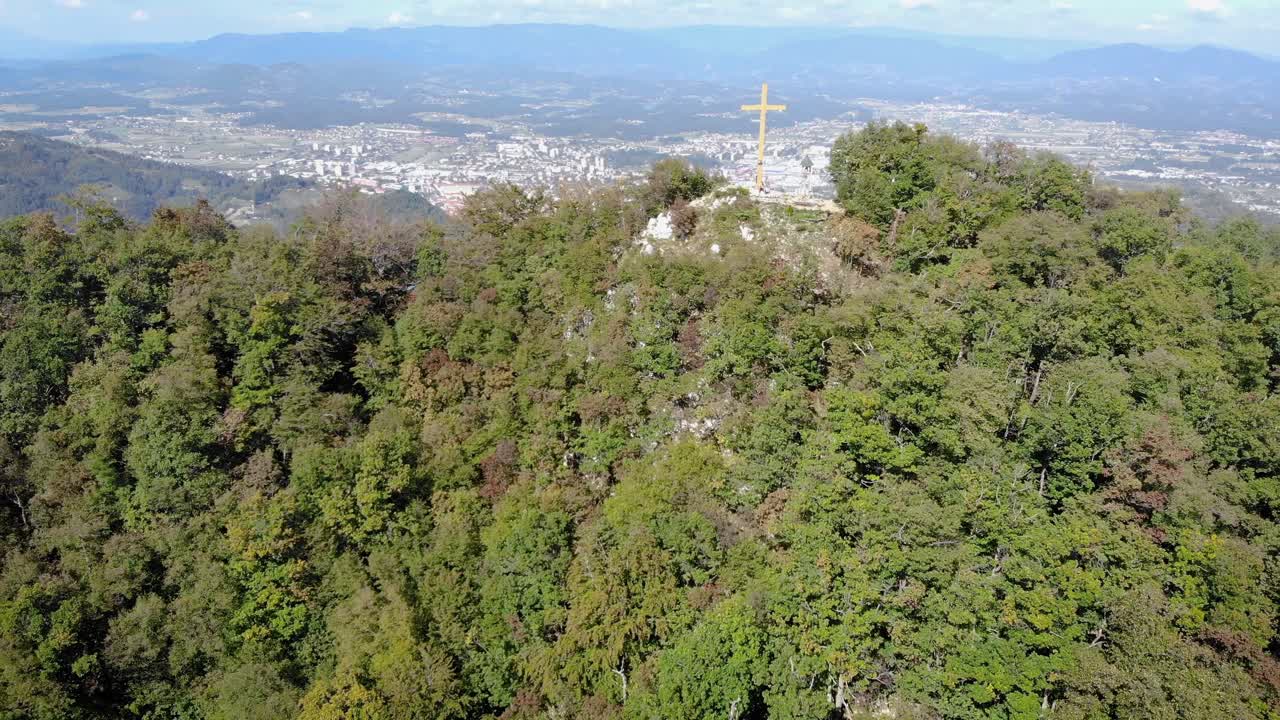 Forward moving aerial over the beautiful Grmada city surrounded by tall mountains with cross sign on the peak. Birds eye view