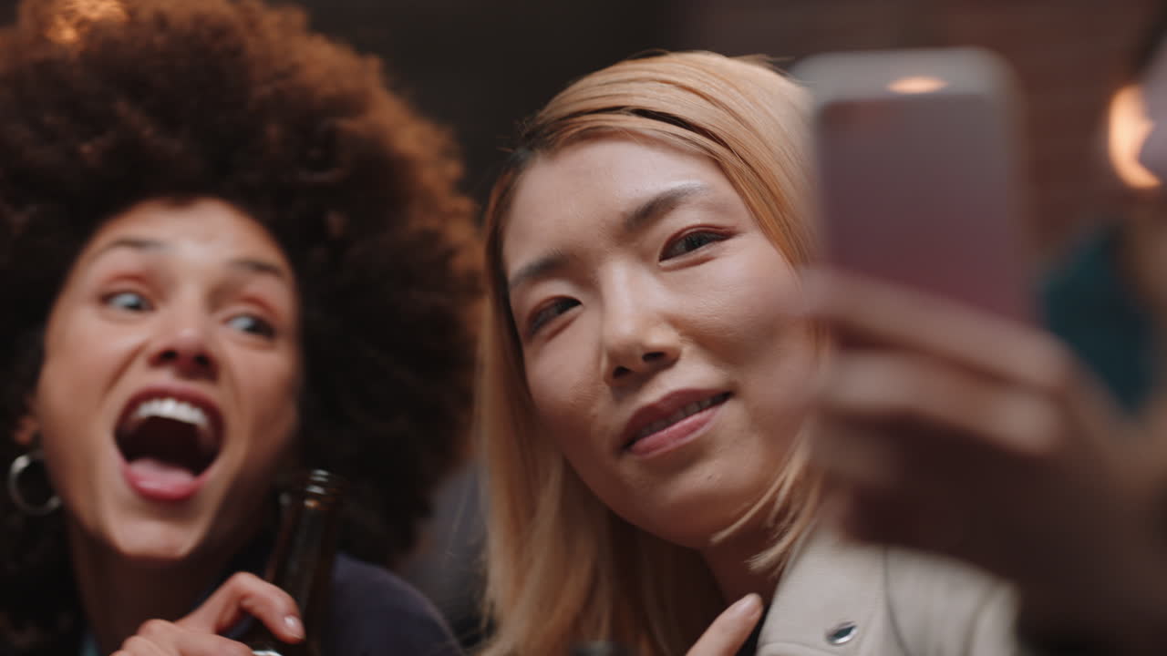 행복한 친구들이 스마트폰을 사용하여 사진을 찍고 축하하고 소셜 미디어에서 축하 파티를 공유하고 함께 추억을 만드는 것을 즐기고 있습니다.