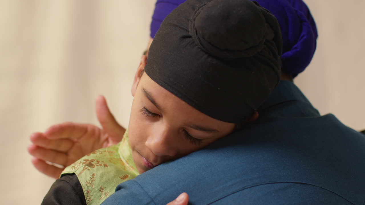 toma de estudio de cerca de un padre sikh abrazando a su hijo ambos con turbantes contra un fondo plano 1