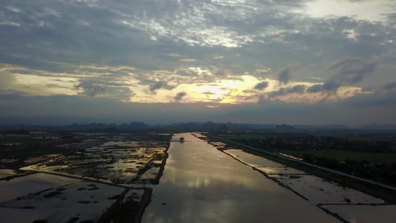 Experience a picturesque sunset in Ninh Binh, Vietnam, with vibrant reflections of the Day River and surrounding wetlands used for plantation, all under a dramatic, colorful sky