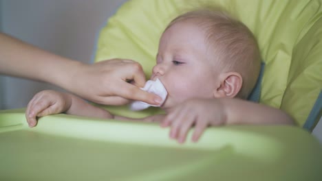 mother cleans baby face feeding boy with soup in highchair