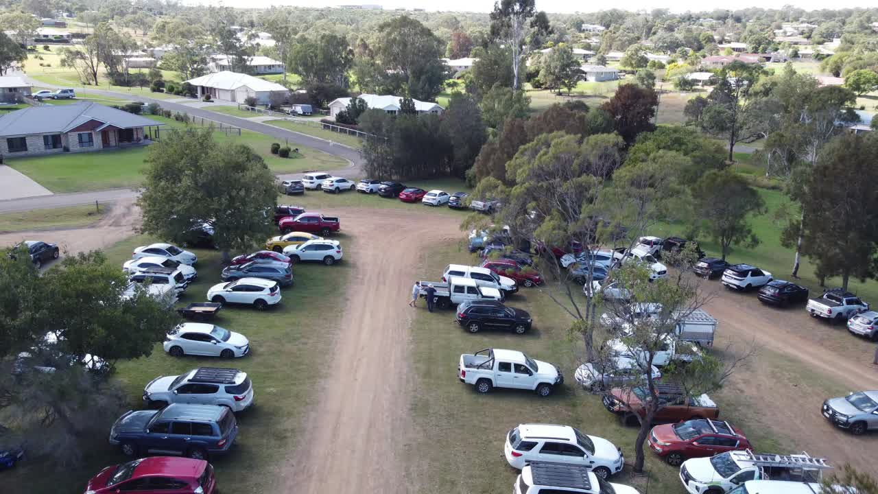 4K video of a drone descending into an unpaved carpark full of parked cars