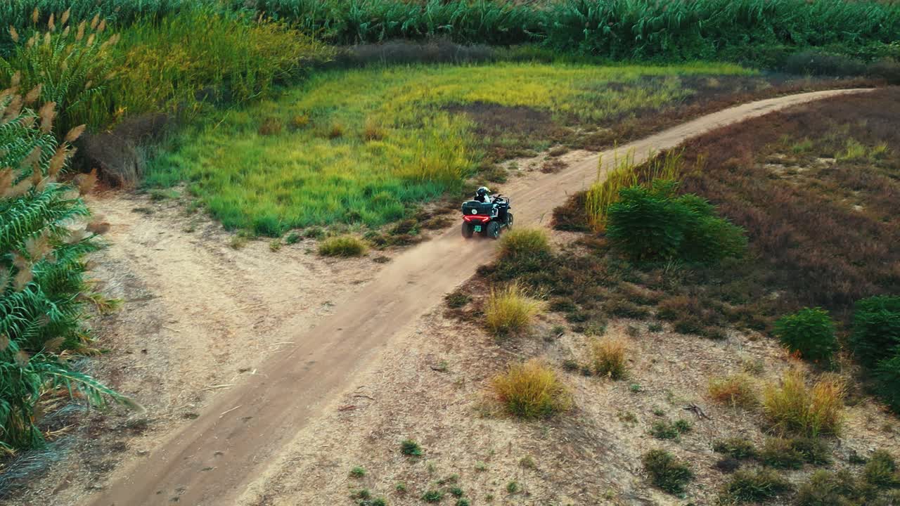 una vista desde arriba, siga el disparo del avión no tripulado de un atv rojo montando en un camino de tierra en un bosque con árboles y campo verde alrededor, video 4k