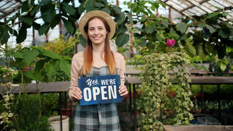woman in a greenhouse holding an open sign