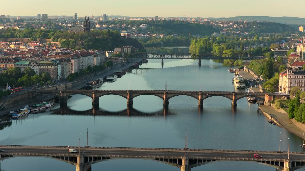 Vista aerea con drone di diversi ponti ad arco che attraversano il fiume Moldava con uno sbarramento in primo piano e la città che si estende fino all'orizzonte all'alba, Praga, Repubblica Ceca.