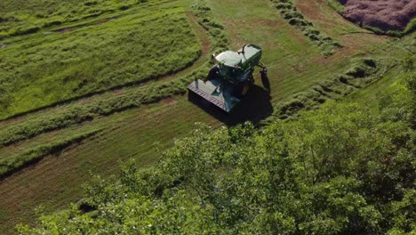 Imágenes-Aéreas-De-Un-Granjero-Cortando-Pasto-Con-Su-Cosechadora-Verde-En-Un-Día-Soleado