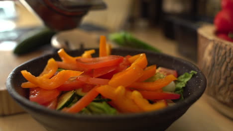 close up of female hands adding sliced pepper to salad bowl