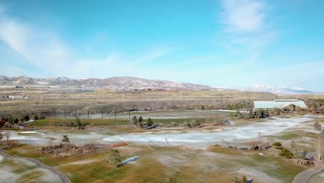 aerial view of a golf course in winter with a light dusting of snow on the ground, mountains in the background and wind turbines