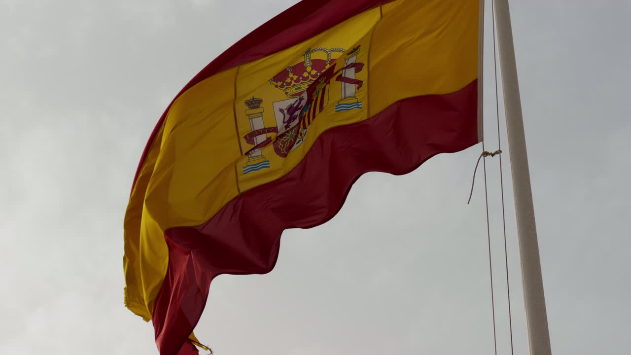 Bandiera nazionale della Spagna che sventola su un'asta contro il cielo. Bandiera spagnola rossa e gialla con stemma che si muove nel vento.