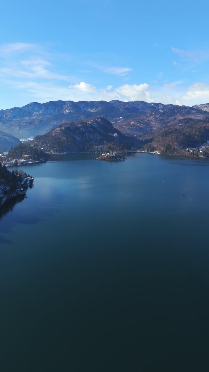 Verticale - Lago di Bled e Isola di Bled in Slovenia, circondati da montagne innevate in inverno. Ripresa aerea con movimento tilt-up.