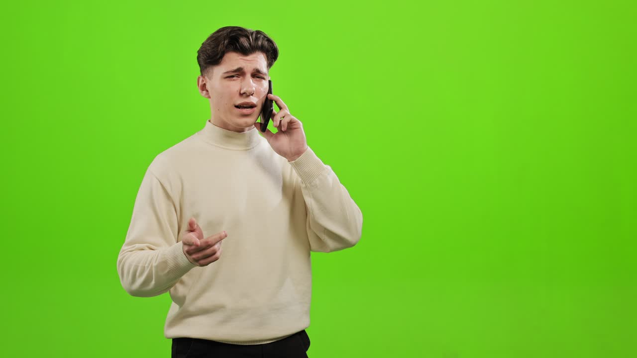 한 남자가 서서 전화를 하고 있다; 그는 진지하고 손을 흔들고 있다; 그는 초록색 바탕에 서 있다; 초록색 화면; 4k.