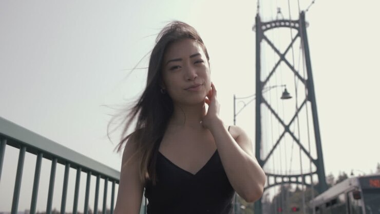 Mezzo primo piano di una donna asiatica che sorride alla telecamera e cammina sul Lions Gate Bridge, in slow motion.