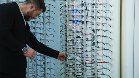 elegant young man looking for modern eyeglasses. male buyer choosing new spectacles at optical store. eyewear concept.