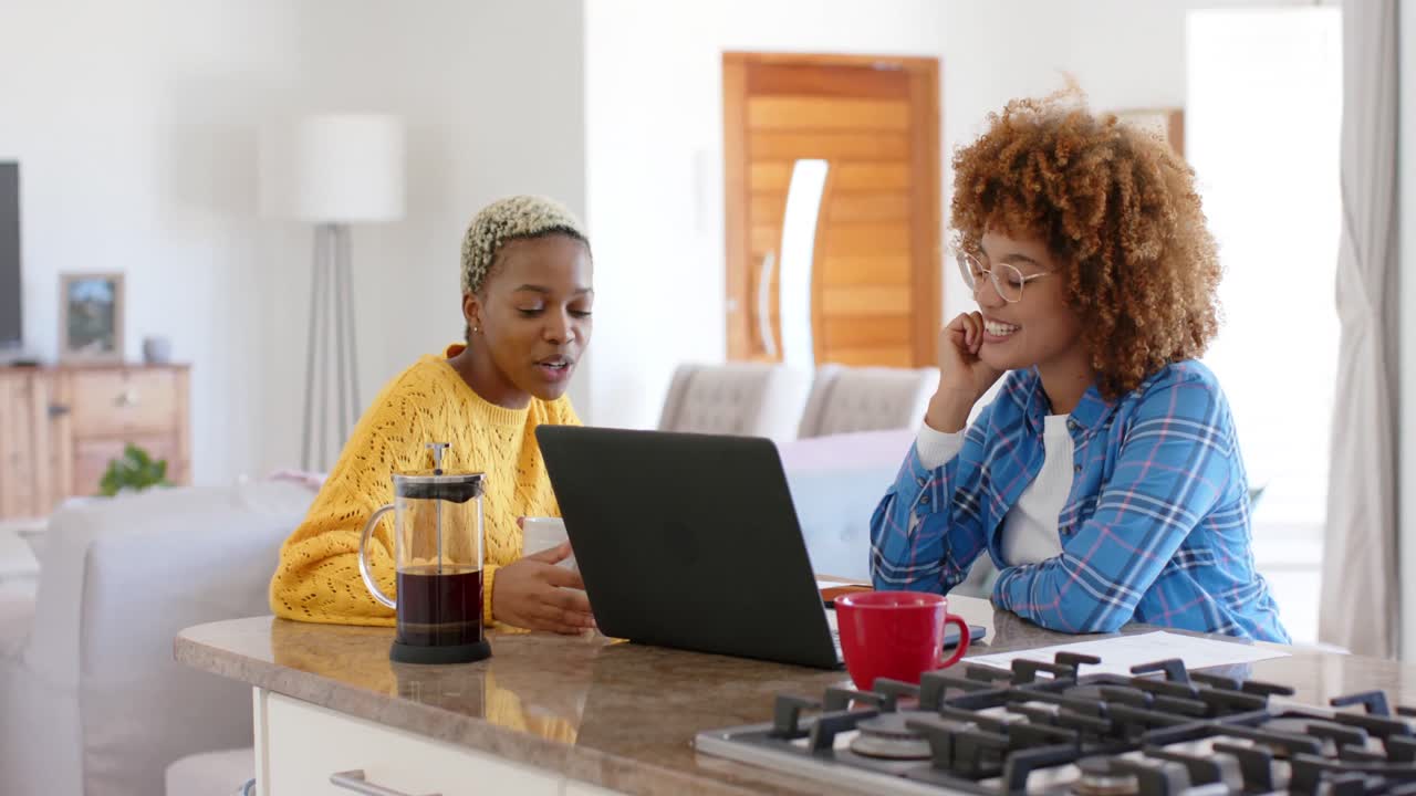 Happy diverse female lesbian couple talking and using laptop in slow motion
