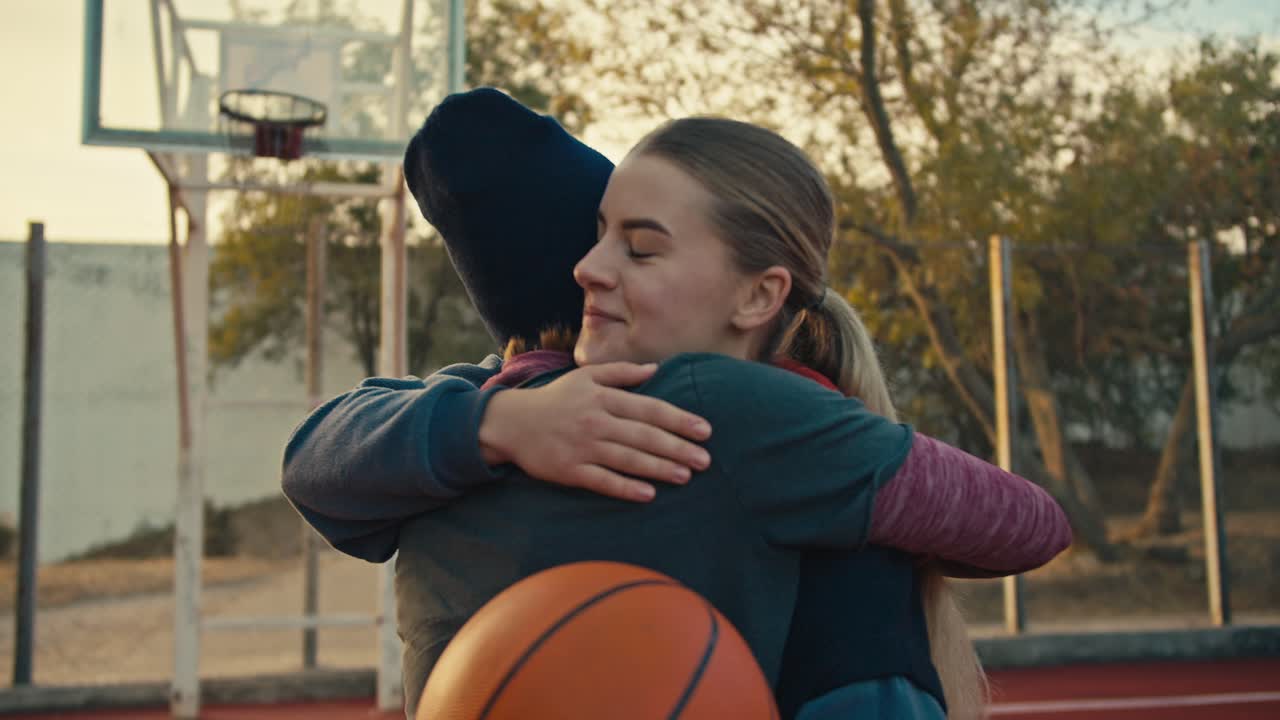 dos chicas rubias felices en ropa deportiva después de jugar al baloncesto se dan unos a otros cinco en la cancha roja en la calle por la mañana. feliz final de entrenamiento y victoria después de jugar a baloncesto en verano