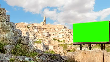 empty billboard with chroma key green screen, panoramic view of typical stones (sassi di matera) and church of matera, european capital of culture 2019, italy, time-lapse, advertisement
