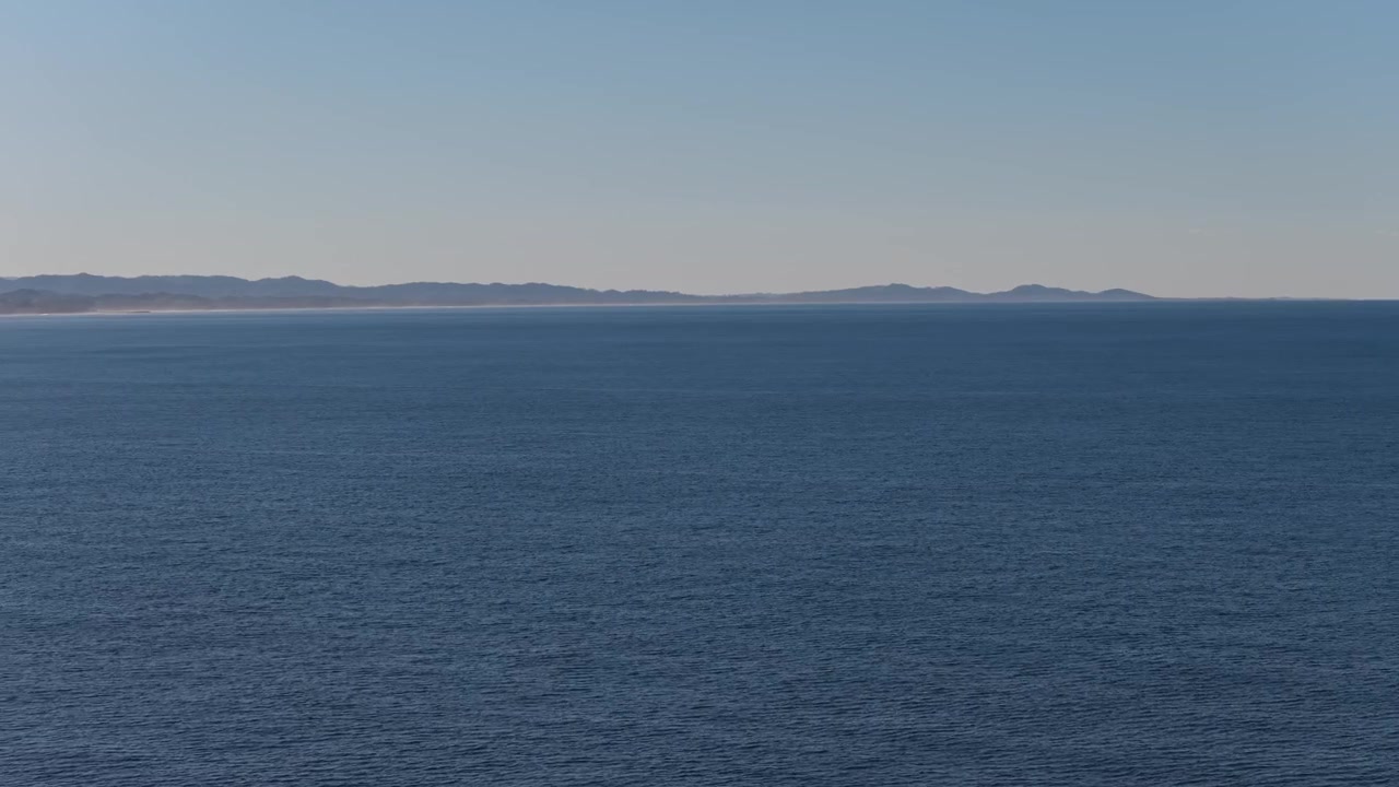 Dybblåt, roligt hav med en klar himmel over i Byron Bay, NSW, Australien. - luftfoto fra siden