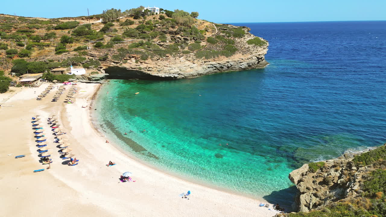 Aerial drone video from iconic sandy beach of Andros with sun beds and umbrellas, Cyclades, Greece