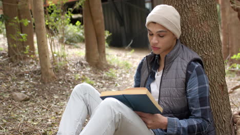 asian man sitting under tree reading book outdoors, enjoying peaceful moment