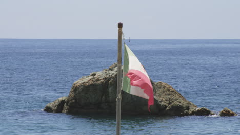 outcrop behind waving flag at monterosso al mare in the province of la spezia, liguria, northern italy