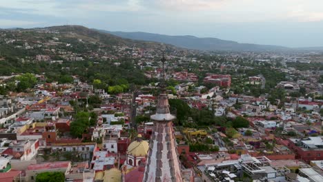 Daytime-Aerial-Cityscape-of-the-Majestic-Cross-atop-Parroquia-de-San-Miguel-Arcangel,-San-Miguel-de-Allende,-dolly-out-pan-left