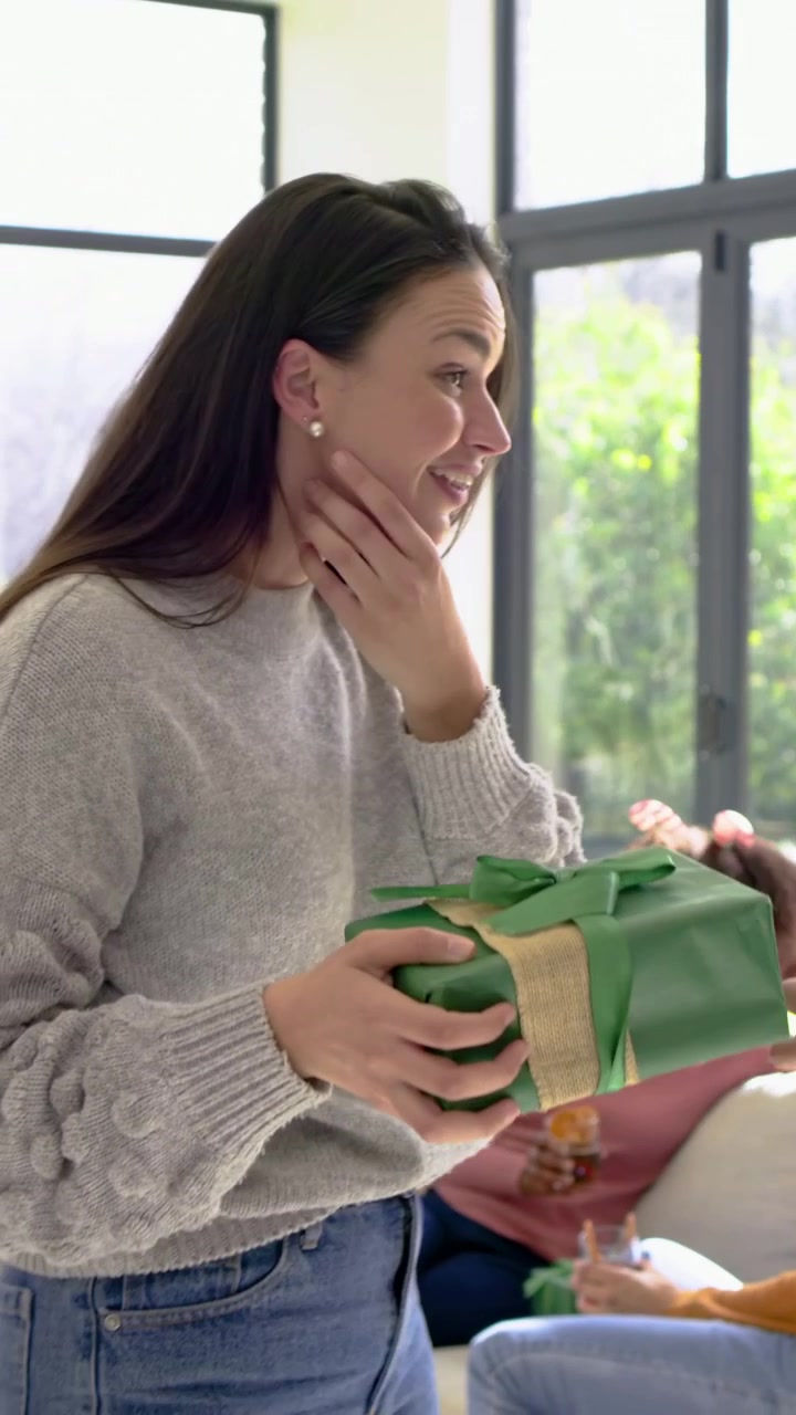 Video verticale: Donna con maglione grigio a casa, mentre inizia lo scambio di regali, offre un regalo verde.