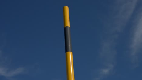 poste amarillo y negro de pie contra un cielo azul claro, con composición minimalista