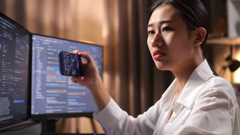 primer plano de una programadora asiática mirando la pantalla de una computadora de escritorio y usando un teléfono inteligente mientras crea ingeniero de software desarrollando aplicaciones, programas, videojuegos en casa