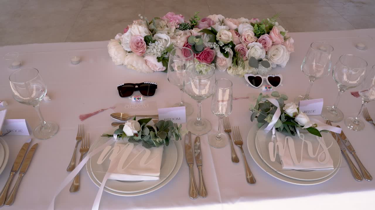 A beautifully arranged wedding table showcases floral centerpieces, glassware, and decorative items in a bright outdoor setting, perfect for a joyful celebration