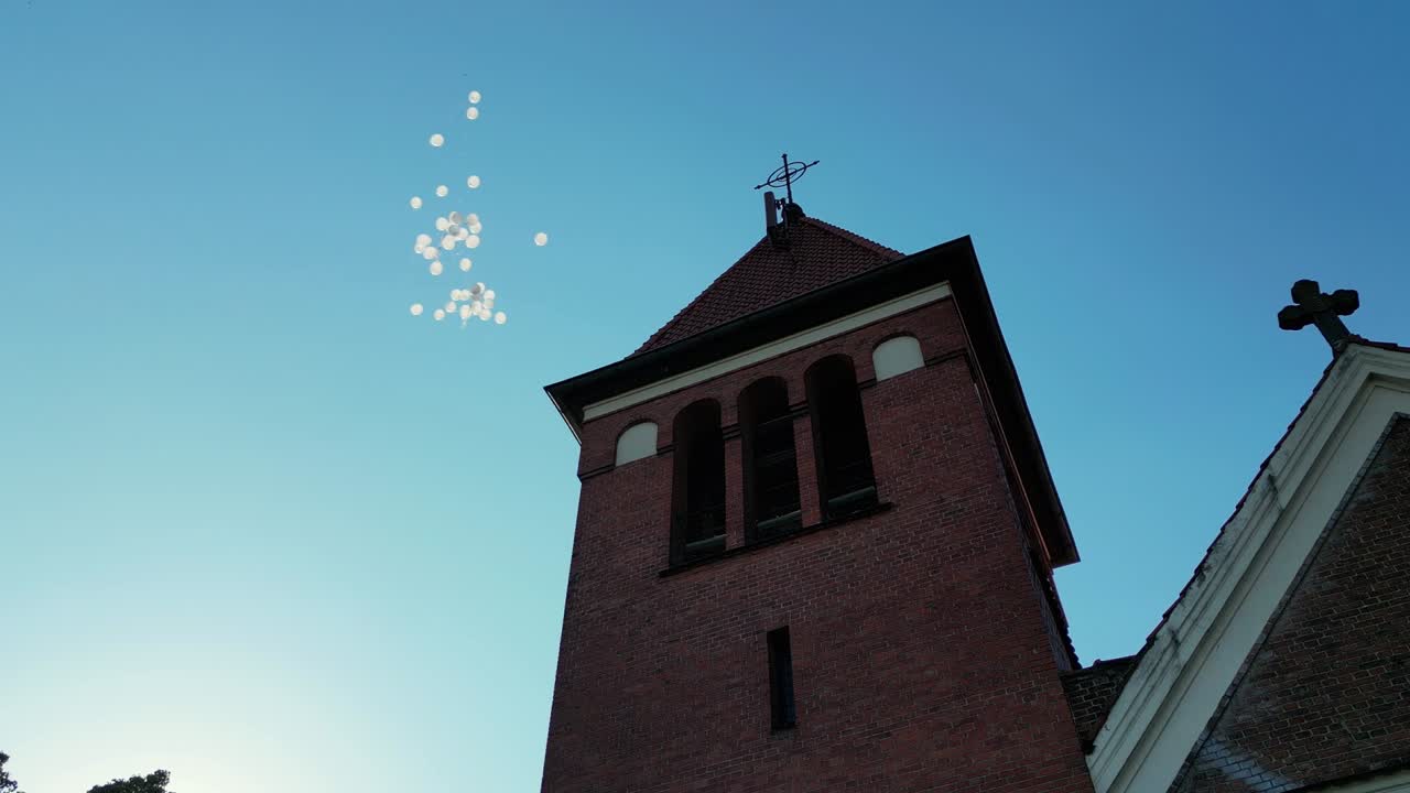 White Balloons Flying into Sky Above Church Tower