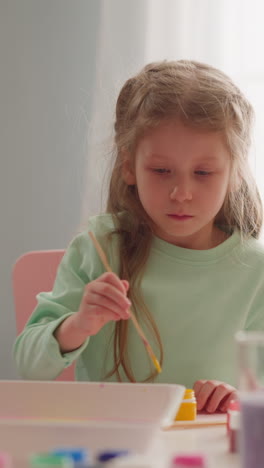 una niña seria dibuja arte ebru con pintura amarilla y se pega con su hermana en el taller en la sala de estar en cámara lenta. pasatiempo de desarrollo para niños